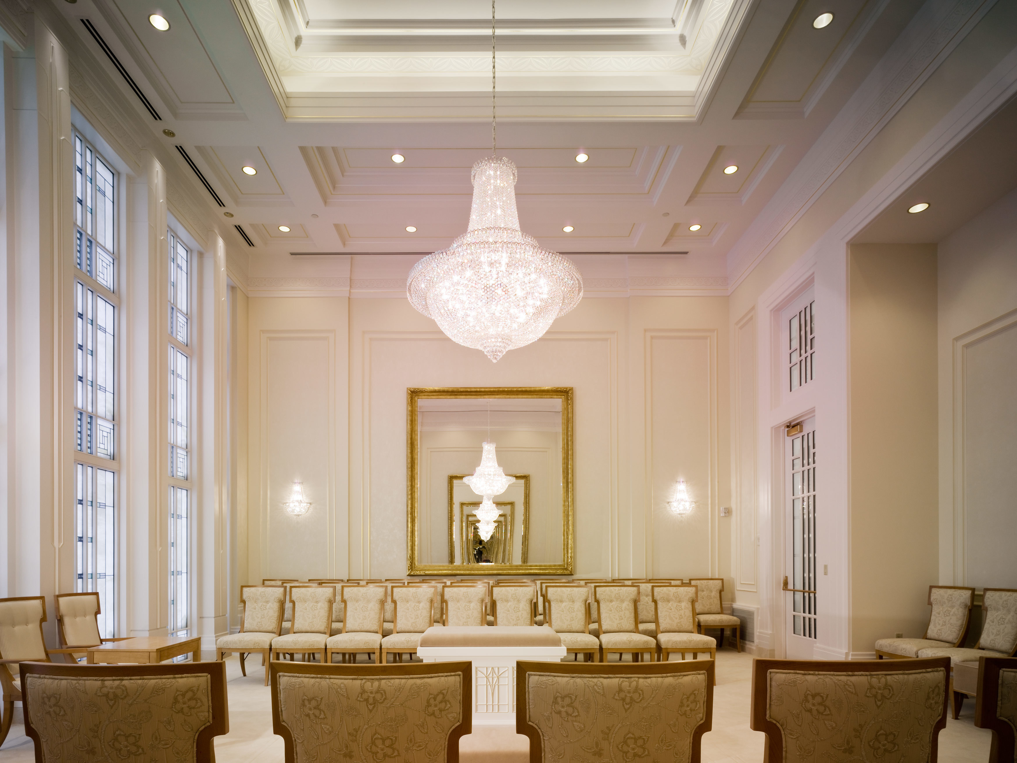A room with rows of white chairs around an altar, with a white chandelier hanging from the ceiling and two mirrors on opposite walls.