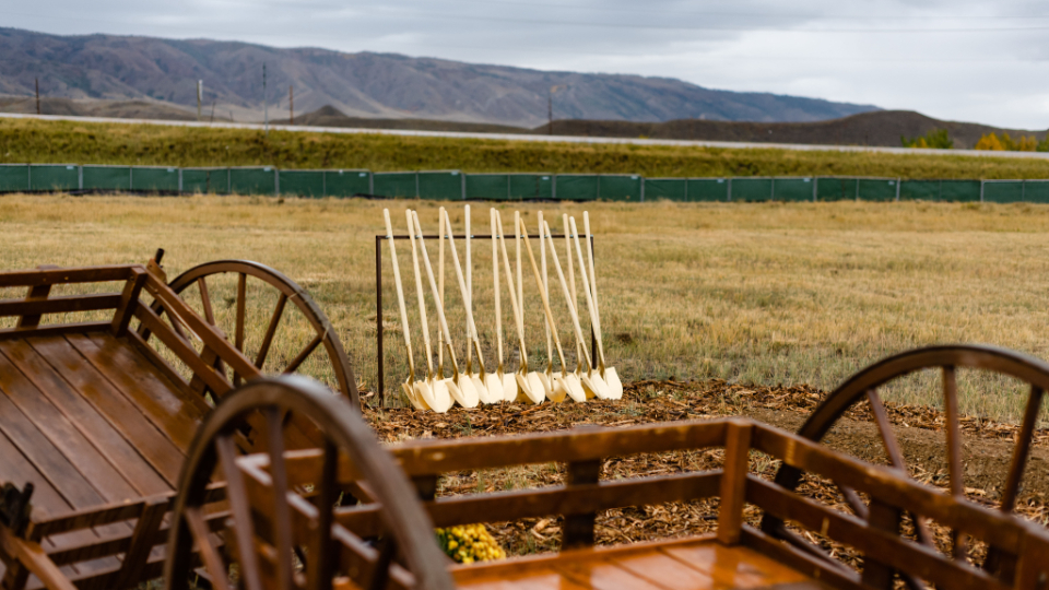 A row of ceremonial golden shovels next to wooden handcart replicas.