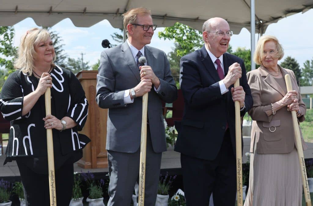 Two men in suits and two women in dresses holding ceremonial golden shovels into the ground.