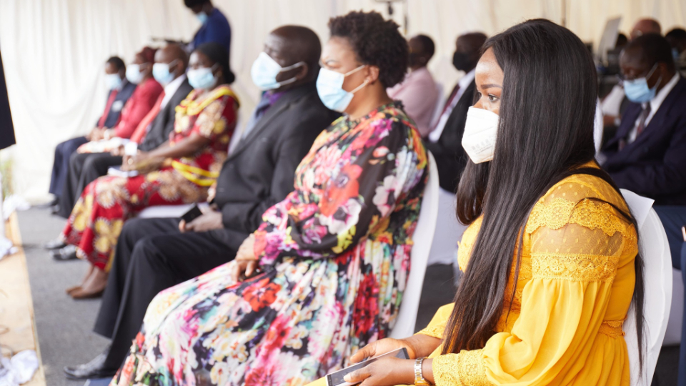 A small congregation of people in Sunday Best sitting on chairs outside and wearing face masks.